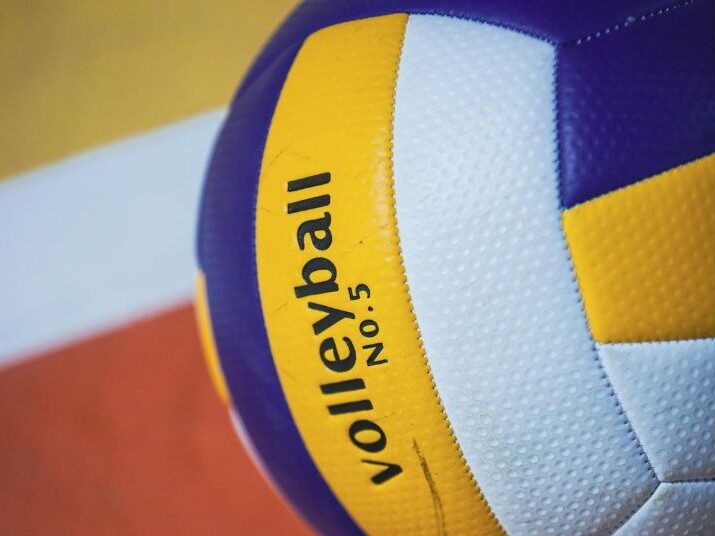 Ein blau-gelb-weiß gestreifter Volleyball liegt auf einem Sporthallenboden. Er ist zirka zur Hälfte im Bild mit der Aufschrift "Volleyball Nummer 5" zu sehen.